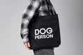 Load image into Gallery viewer, Schwarzer Jutebeutel mit weißem „Dog Person“-Print von Karma Hund, frontal fotografiert.